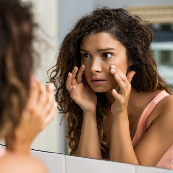 Young woman looking at her face in the mirror. Helping patients create the right anti-aging plan for patients no matter their age
